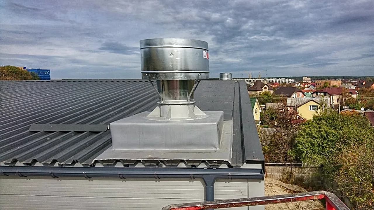 Промисловий даховий вентилятор з металевим дефлектором, змонтований на утепленій основі покрівлі з профнастилу.