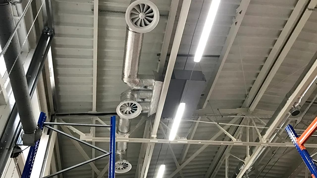 Монтажник на будівельній вишці-турі встановлює внутрішній канальний блок Haier під перекриттям складу.