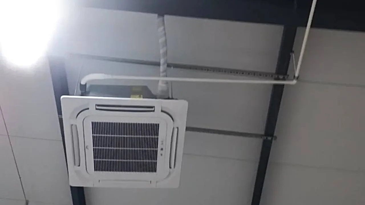 Cassette air-conditioning unit with drain and refrigerant lines connected, fixed to the steel ceiling frame.